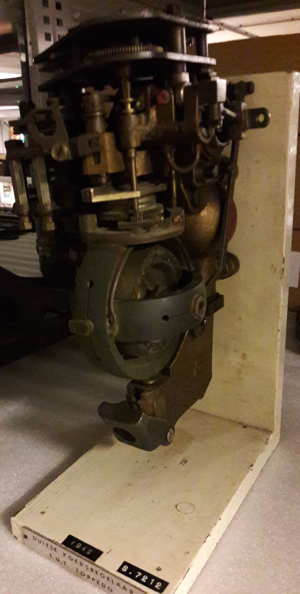 Koersregelaar van een Duitse L.U.T torpedo. Brons en staal gemonteerd op wit geschilderde houten plank.